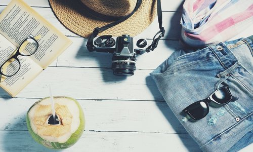 Bild zeigt sommerliche Attribute wie Sonnenbrille, Cocktail, Sommerhose und Buch