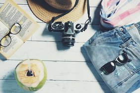 Bild zeigt sommerliche Attribute wie Sonnenbrille, Cocktail, Sommerhose und Buch